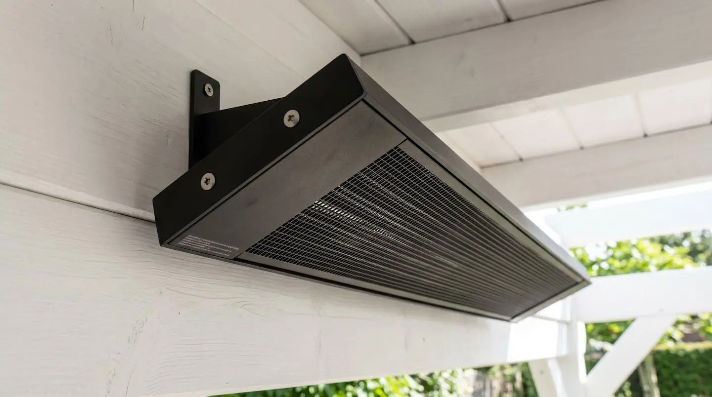 Radiateur infrarouge extra-plat noir mat installé sous plafond de pergola blanche, design discret et finition aluminium