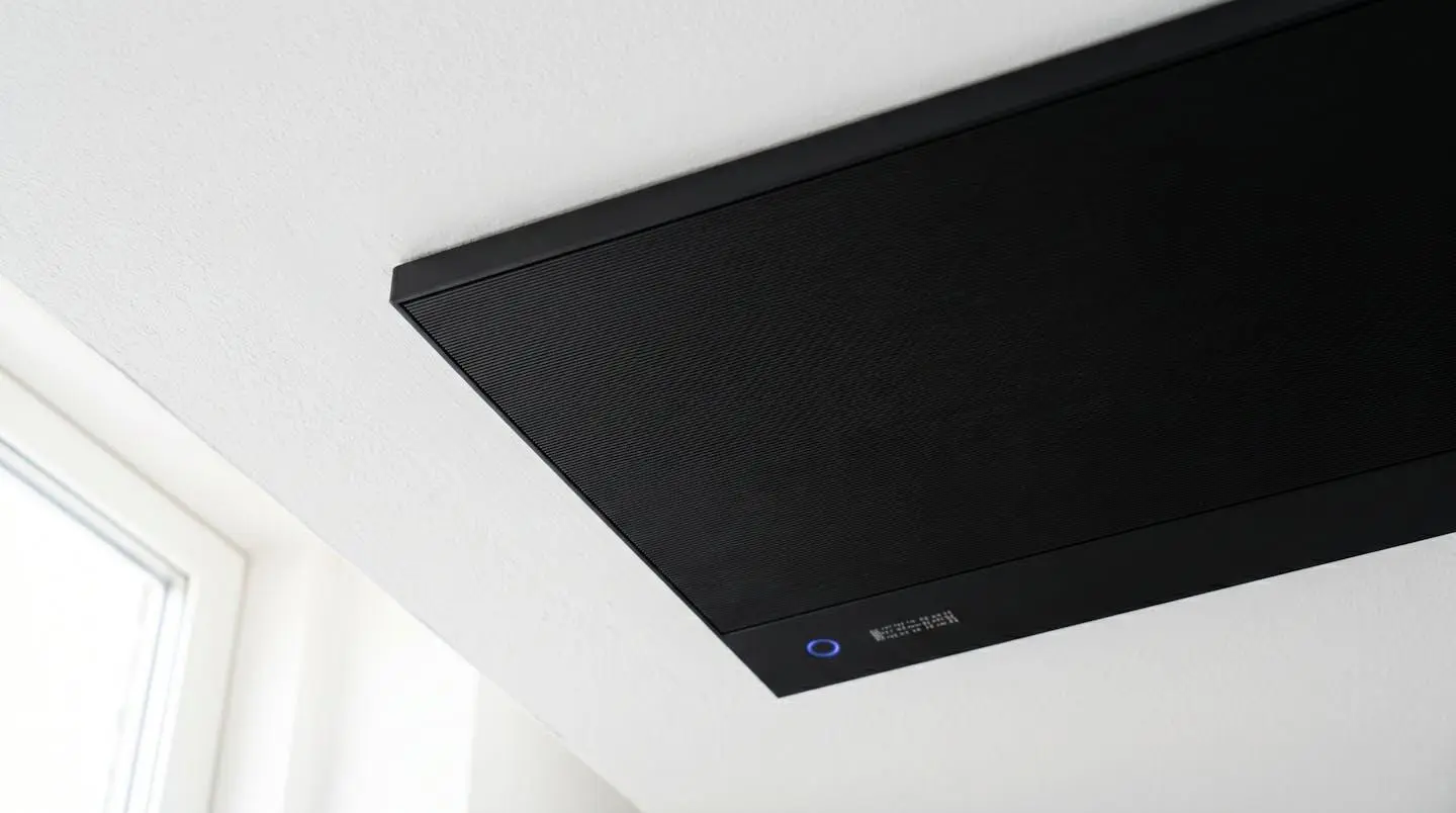 Gros plan d'un radiateur infrarouge extra-plat noir mat fixé au plafond blanc, finition contemporaine avec discret voyant LED bleu, tout net en profondeur de champ